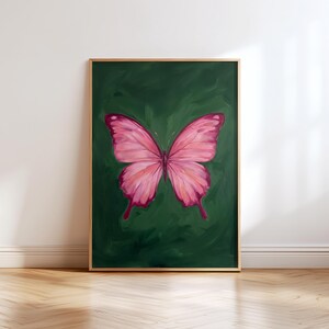 May include: A framed painting of a pink butterfly against a dark green background. The butterfly has detailed wing patterns and is centered in the frame. The artwork is displayed on a wall with a wooden floor.