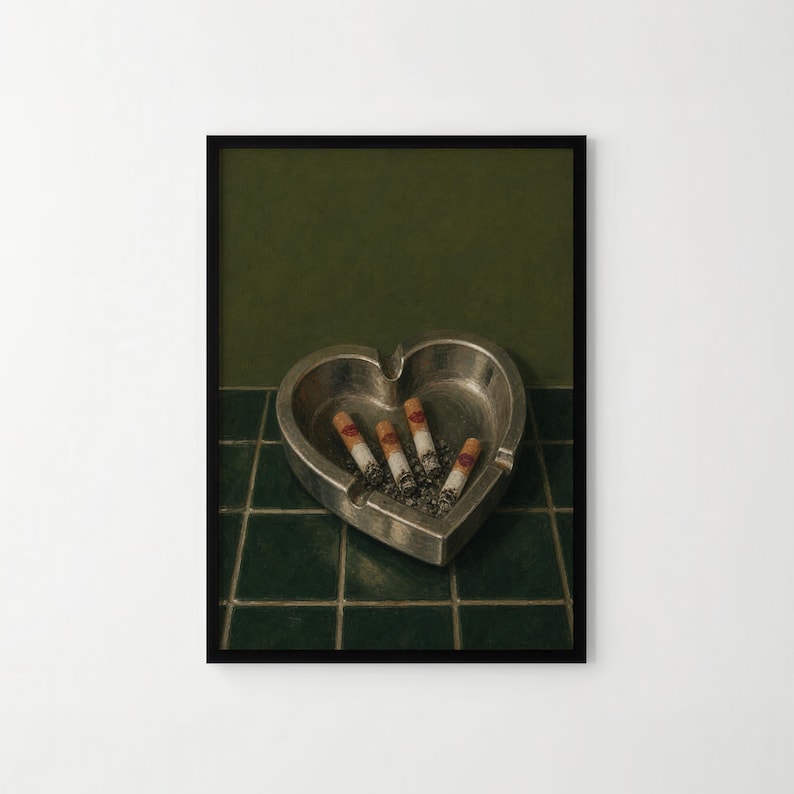 May include: A heart-shaped silver metal ashtray containing four cigarette butts, each featuring a small red lipstick kiss mark on the filter. The ashtray is positioned on a dark green tiled surface against a solid dark green background.