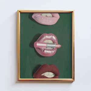 May include: A framed artwork showing three sets of lips in shades of pink and red against a dark green backdrop. One set of lips holds a pink lipstick. The artwork is presented in a gold-coloured frame.