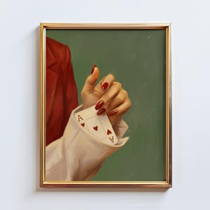 Peut inclure: Impression artistique encadrée d'une main tenant deux cartes à jouer, deux As de Coeur. La main vernie de rouge sort d'une manchette de chemise blanche. Une veste rouge est visible à gauche, sur fond vert.