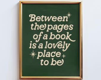 May include: A framed print with the text "Between the pages of a book is a lovely place to be" in a cream-colored, whimsical font. The text is set against a dark green background, framed by a gold-colored border.