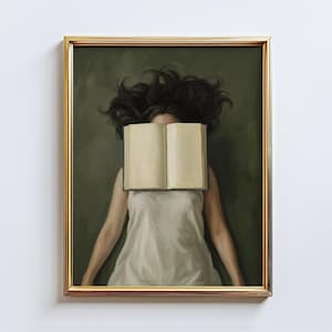 May include: A framed art print featuring a person with dark hair and a white dress, with an open book covering their face. The artwork has a gold frame and a green background.