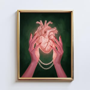 May include: A framed artwork featuring a glowing anatomical heart held by two hands with red nails. A double strand of pearls adorns the hands. The background is a dark green, and the frame is gold.
