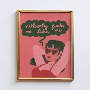 May include: A framed art print featuring a woman with heart-shaped sunglasses, arms behind her head, and the text "nobody fucks me like me" in a green speech bubble. The artwork has a pink background and a gold frame.