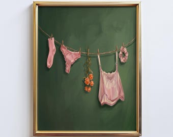 Könnte beinhalten: Ein gerahmtes Kunstwerk zeigt eine Wäscheleine mit rosa Dessous, einer Socke und einem Haargummi vor einem dunkelgrünen Hintergrund. Ein kleiner Strauß orangefarbener Rosen ist ebenfalls an der Leine befestigt. Das Kunstwerk ist in einem goldfarbenen Rahmen gerahmt.