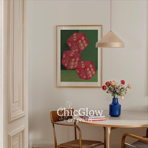 May include: A framed art print featuring three red dice with white dots against a green background. The artwork is displayed in a room with a round table, a blue vase of flowers, and a pendant light.
