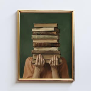 May include: A framed art print featuring a stack of vintage books held by hands, with the books obscuring the face. The books are various shades of brown and tan, set against a dark green background. The frame is gold.