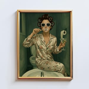 May include: A framed print depicts a person in pajamas, sunglasses, and hair curlers brushing their teeth while holding a martini. The person is seated on a bathroom sink. The pajamas have a floral pattern.