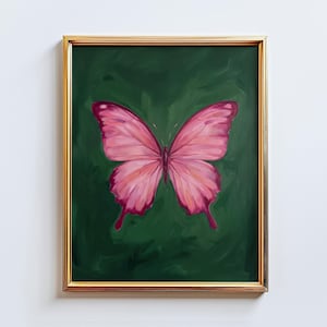 May include: A framed painting featuring a pink butterfly against a dark green background. The butterfly has detailed wing patterns with shades of pink and red. The frame is gold-colored, adding a touch of elegance to the artwork.