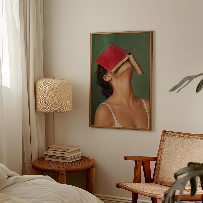 Puede incluir: Una impresi&oacute;n art&iacute;stica enmarcada representa a una persona con un libro rojo cubriendo su rostro, sobre un fondo verde. La persona lleva una camiseta sin mangas blanca. La obra de arte est&aacute; en una habitaci&oacute;n con una l&aacute;mpara y una mesita.