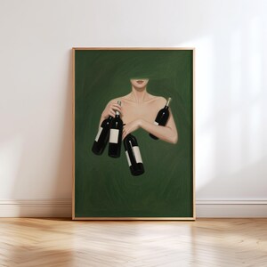 May include: Art print featuring a woman holding several wine bottles against a dark green background. The bottles are black with white labels. The artwork is framed in a gold-colored frame and is displayed on a white wall.