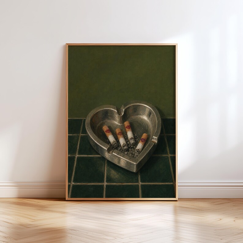 May include: A heart-shaped metallic ashtray containing four cigarette butts with visible red filter markings. The ashtray is positioned on a dark green tiled surface against a solid dark green wall, creating a monochromatic color scheme.