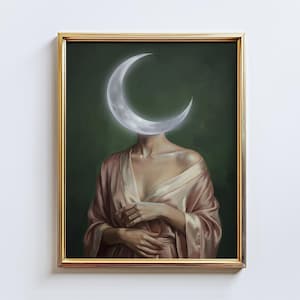 May include: A framed artwork featuring a figure with a crescent moon replacing the head. The figure wears a pink satin robe against a dark green background. The artwork is framed in a gold-colored frame.