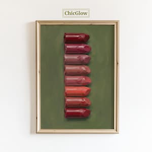 May include: A framed art print featuring a vertical arrangement of eight lipsticks in varying shades of red and pink against a green background. The artwork is framed in a light wood frame, with the text "ChicGlow" at the top.