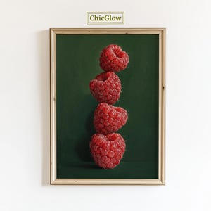 Pode incluir: Uma impressão emoldurada com quatro framboesas vermelhas empilhadas verticalmente contra um fundo verde escuro. As framboesas são detalhadas, com texturas visíveis e uma cor vibrante. A impressão tem uma moldura dourada e o texto "ChicGlow" no canto superior.