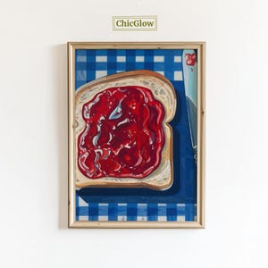 May include: A framed art print featuring a slice of toast generously covered with red jam, resting on a blue and white checkered tablecloth. A silver knife with a red jam smear is next to the toast. The text "ChicGlow" is in the top left corner.