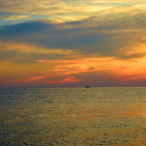 Puede incluir: Una puesta de sol escénica sobre un océano tranquilo con dos pequeños barcos en la distancia. El cielo es una mezcla de naranja, rosa y azul con nubes tenues.