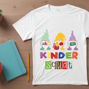 Puede incluir: Camiseta blanca con un gr&aacute;fico de tres gnomos con sombreros y sosteniendo carteles que dicen "ABC", "123" y una mochila. El texto "Kinder Squat" est&aacute; impreso debajo de los gnomos.