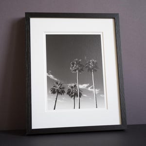 Könnte beinhalten: Eine weiße Keramik-Tasse mit schwarzem Henkel und dem Text "But First, Coffee" in schwarzer, fetter Schrift. Die Tasse steht auf einer Holzoberfläche. Die Tasse ist etwa 10 cm hoch.