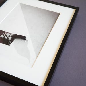 May include: A black and white framed print featuring a silhouette of a cat resting near a window frame. The artwork is encased in a thin black frame with a white mat border, creating a high-contrast composition with sharp geometric shadows.