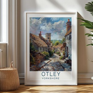 Puede incluir: Un cartel de viaje vintage que presenta una vista pintoresca de una calle empedrada en Otley, Yorkshire. La calle está bordeada de encantadores edificios de piedra, incluida una iglesia con un alto campanario. El cielo es azul brillante con nubes blancas esponjosas.
