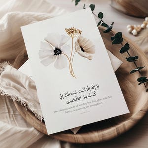 以下が含まれることがあります： 水彩画の花のアートとアラビア書道が施された白いグリーティングカード。カードには、金色の茎を持つ白とベージュの花が描かれています。テキストは「あなた以外に崇拝に値する者はなく、あなたに栄光があります」と書かれています。