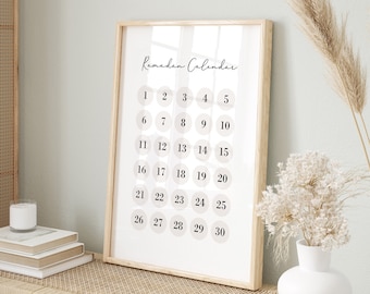 May include: A framed Ramadan Calendar print with a light wood frame. The calendar features a minimalist design with numbers 1-30 in a grid, each within a light beige circle. The words "Ramadan Calendar" are written in a script font at the top.