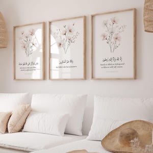Può includere: Tre stampe artistiche incorniciate con disegni floreali e calligrafia araba. Ogni stampa presenta una cornice in legno chiaro, uno sfondo bianco e delicati fiori rosa e bianchi. Le stampe mostrano citazioni ispiratrici in arabo e inglese.