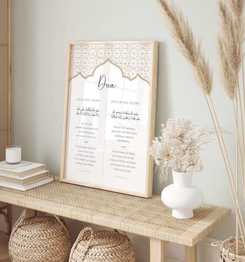 Puede incluir: Una impresi&oacute;n enmarcada con un fondo beige y un patr&oacute;n geom&eacute;trico. La impresi&oacute;n presenta la palabra "Dua" en una fuente decorativa e incluye texto &aacute;rabe y traducciones al ingl&eacute;s para salir y entrar a una casa. El texto dice "Bismillahi walajna, wakala rabbina tawakkalna" y "Bismillahi tuwakkaltu ala Allahi, wa la hawla wa la quwwata illa billah".