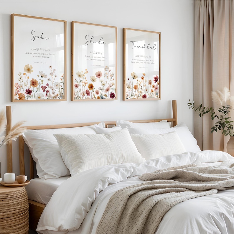 May include: Three framed wall art pieces with floral designs and calligraphy. The frames are light brown, and the artwork features a variety of flowers in shades of red, yellow, and white. The calligraphy is in black. The art is displayed above a bed with white bedding.