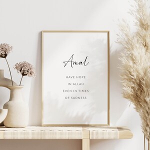 K&ouml;nnte beinhalten: Ein gerahmter Druck mit einem goldenen Rahmen und wei&szlig;em Hintergrund. Der Druck zeigt das Wort "Amal" in Kursivschrift und den Text "Have hope in Allah even in times of sadness". Der Druck wird auf einem Regal mit einer Vase mit Trockenblumen und einer hohen Vase mit Pampasgras angezeigt.