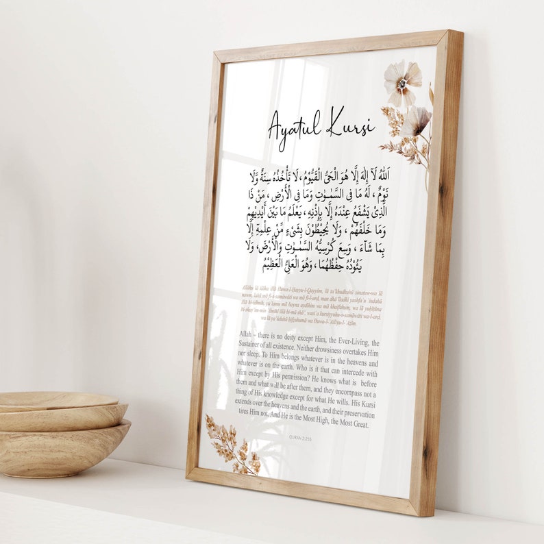 Puede incluir: Una impresi&oacute;n enmarcada con un fondo beige y acentos florales marrones. La impresi&oacute;n presenta el texto &aacute;rabe de Ayatul Kursi, un vers&iacute;culo del Cor&aacute;n, con una traducci&oacute;n al ingl&eacute;s debajo. El marco es de madera con un acabado marr&oacute;n claro.