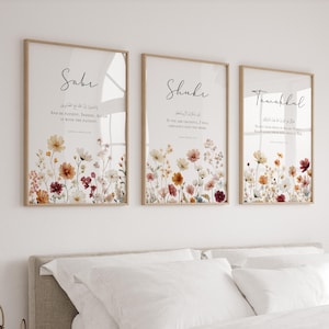 May include: Three framed art prints with floral designs and calligraphy. Each print features a different word: "Saber," "Shukr," and "Tawakkul." The floral arrangements include white, yellow, orange, and burgundy flowers. The frames are a light brown color.