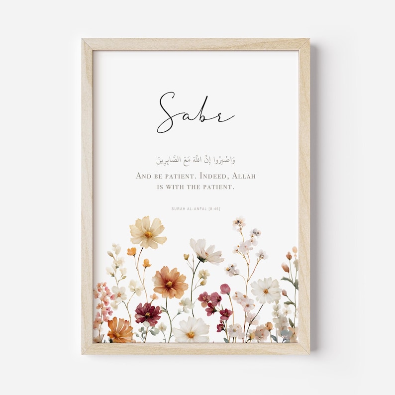 May include: A framed print featuring the word "Sabr" in elegant script above Arabic text and English translation: "And be patient. Indeed, Allah is with the patient." The bottom of the print is adorned with a floral arrangement in warm tones.