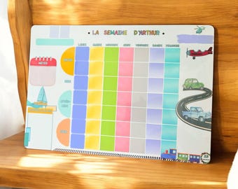 May include: A rectangular magnetic weekly planner board titled LA SEMAINE D'ARTHUR featuring a colorful grid for days of the week and times of day. The board includes illustrations of a red airplane, a green car, a blue truck, and a train.