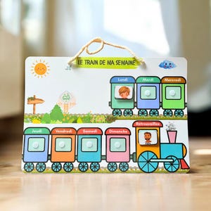 Op de afbeelding: Een kleurrijk houten educatief speelgoed met een treinthema. Het bord toont de dagen van de week met treinwagons, elk met een knop. De tekst "LE TRAIN DE MA SEMAINE" staat bovenaan. Inclusief een zon, wolk en andere afbeeldingen.