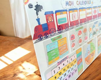 May include: A white magnetic calendar board titled Mon Calendrier featuring a red train illustration with a lion in the engine. The board includes colorful sections for months, days, and dates with numbers 1 through 31 and French text labels.