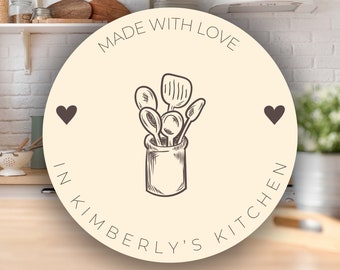 May include: A round, cream-colored kitchen sign with the text "MADE WITH LOVE IN KIMBERLY'S KITCHEN" encircling a drawing of kitchen utensils in a jar. Two dark brown hearts flank the central image.