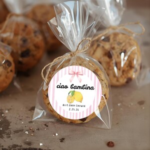 May include: Chocolate chip cookies individually wrapped in clear cellophane, tied with twine. Each cookie has a round sticker with pink stripes, a bow, lemons, and the text "Ciao Bambina, Ali's Baby Shower 2.25.26."