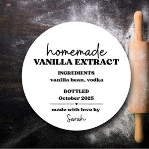 May include: A white circular label with the text "homemade VANILLA EXTRACT" and ingredient details. The label includes "vanilla bean, vodka" and "October 2025". A wooden rolling pin is on the right side of the image.