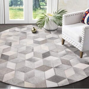 May include: A round, gray and white cowhide rug with a geometric pattern. The rug is made of natural cowhide and has a unique, rustic look.