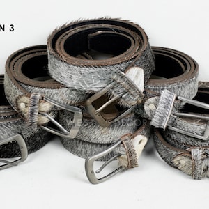 May include: Several rolled leather belts with silver-toned buckles. The belts have a gray and white speckled fur-like texture. The image includes the text "OPTION 3" in the upper left corner and a logo in the upper right corner.