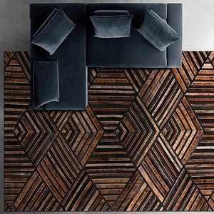 May include: A geometric patterned rug with brown and black leather strips. The rug is under a dark blue sectional sofa with three cushions.