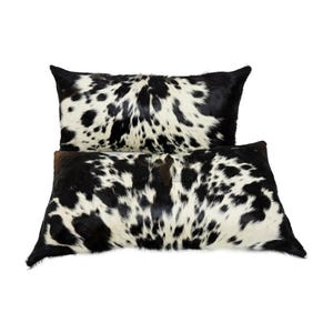 May include: Two black and white cowhide throw pillows. The pillows are rectangular and have a soft, plush texture.