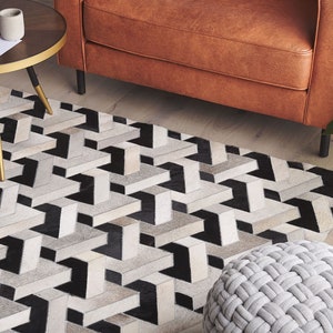 May include: A black, white, and gray geometric patterned rug with a brown leather sofa and a round gold table in the background.