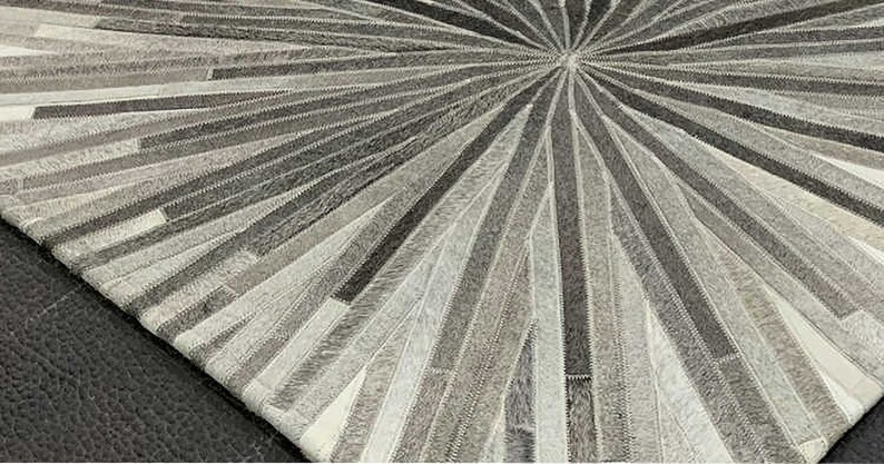Pu&ograve; includere: Un tappeto in pelle di mucca grigio e bianco con un design circolare. Il tappeto &egrave; realizzato con strisce di pelle cucite insieme per creare un motivo a raggiera.
