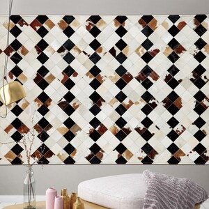 Puede incluir: Una alfombra de piel de vaca negra, blanca y marrón con un patrón de diamantes. La alfombra está hecha de piezas individuales de piel de vaca que se han cosido juntas.