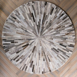 Pode incluir: Um tapete redondo de pele de vaca cinza e branco com um padrão circular de tiras que irradiam do centro.