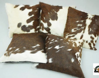May include: Five brown and white cowhide throw pillows with a Wild West Decor logo in the bottom right corner.