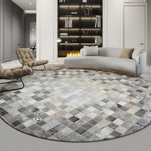 May include: A round, gray and white cowhide rug with a geometric pattern. The rug is in a living room setting with a white sofa and two chairs.